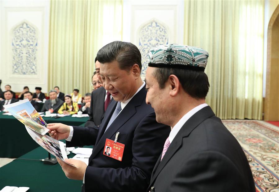 Chinese President Xi Jinping looks at photos of the family of Kurban Tulum when joining a panel discussion with deputies to the 12th National People